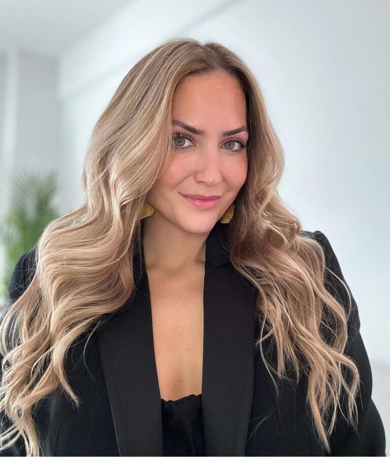 Woman with long wavy blonde hair wearing a black blazer.