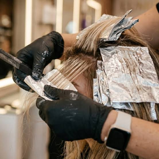 Hairdresser applying foil for highlights on client's blonde hair.