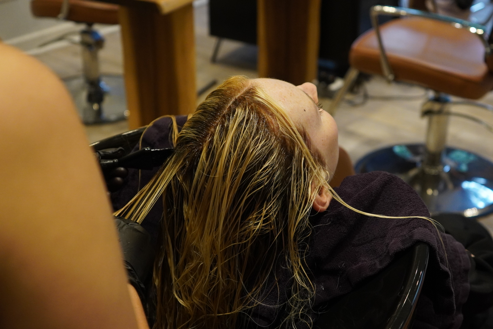 Person receiving a hair treatment at a salon, with stylist applying product to wet hair.