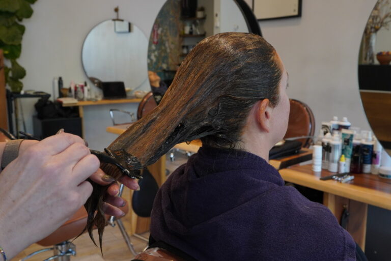 Person receiving a hair treatment in a salon, with stylist applying product to wet hair.