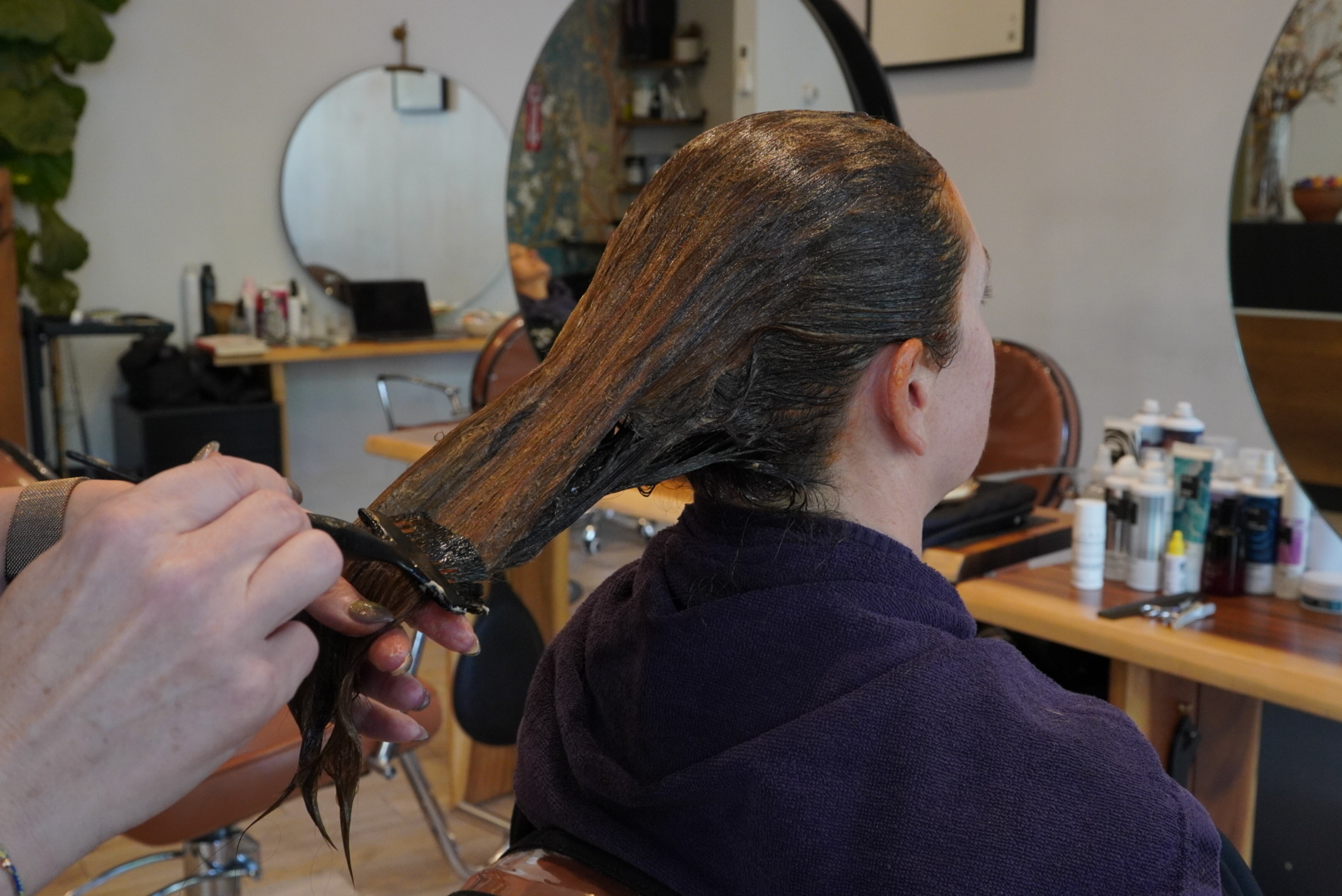 Person receiving a hair treatment in a salon, with stylist applying product to wet hair.