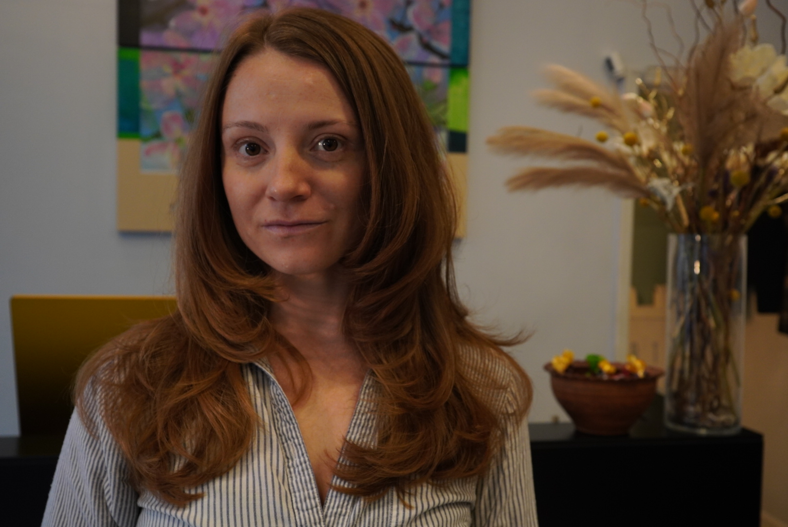 Woman with long hair standing in a room with art and dried flowers.