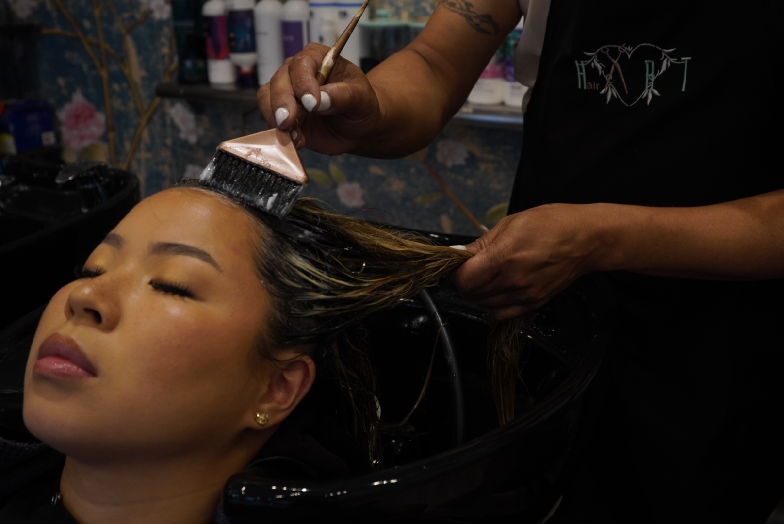 Person receiving hair coloring treatment at a salon, stylist applying dye with a brush.
