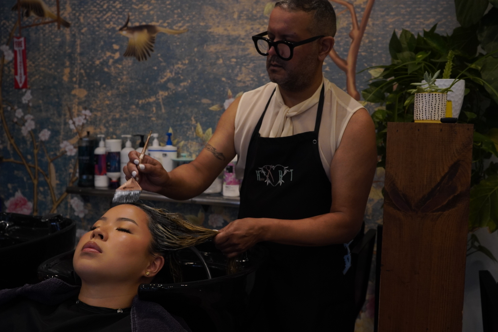 Person getting hair treatment in a salon with floral wallpaper background.