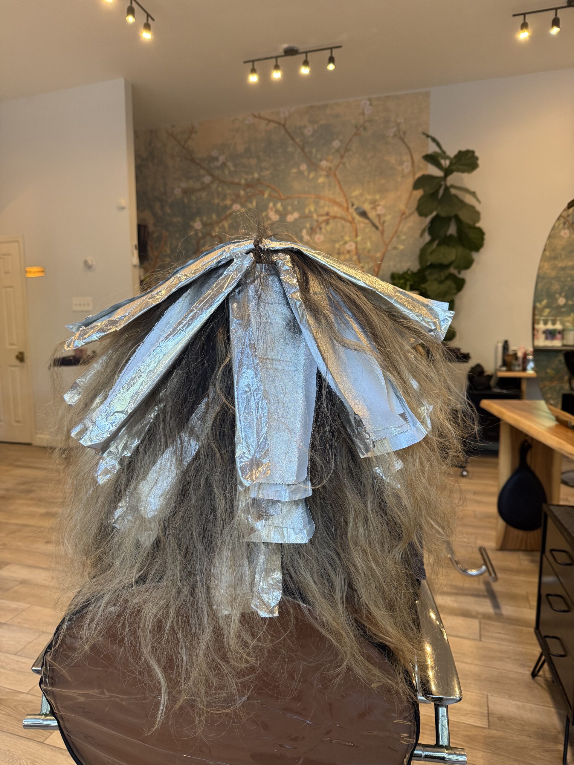 Person with hair in foils undergoing a highlighting process in a salon.