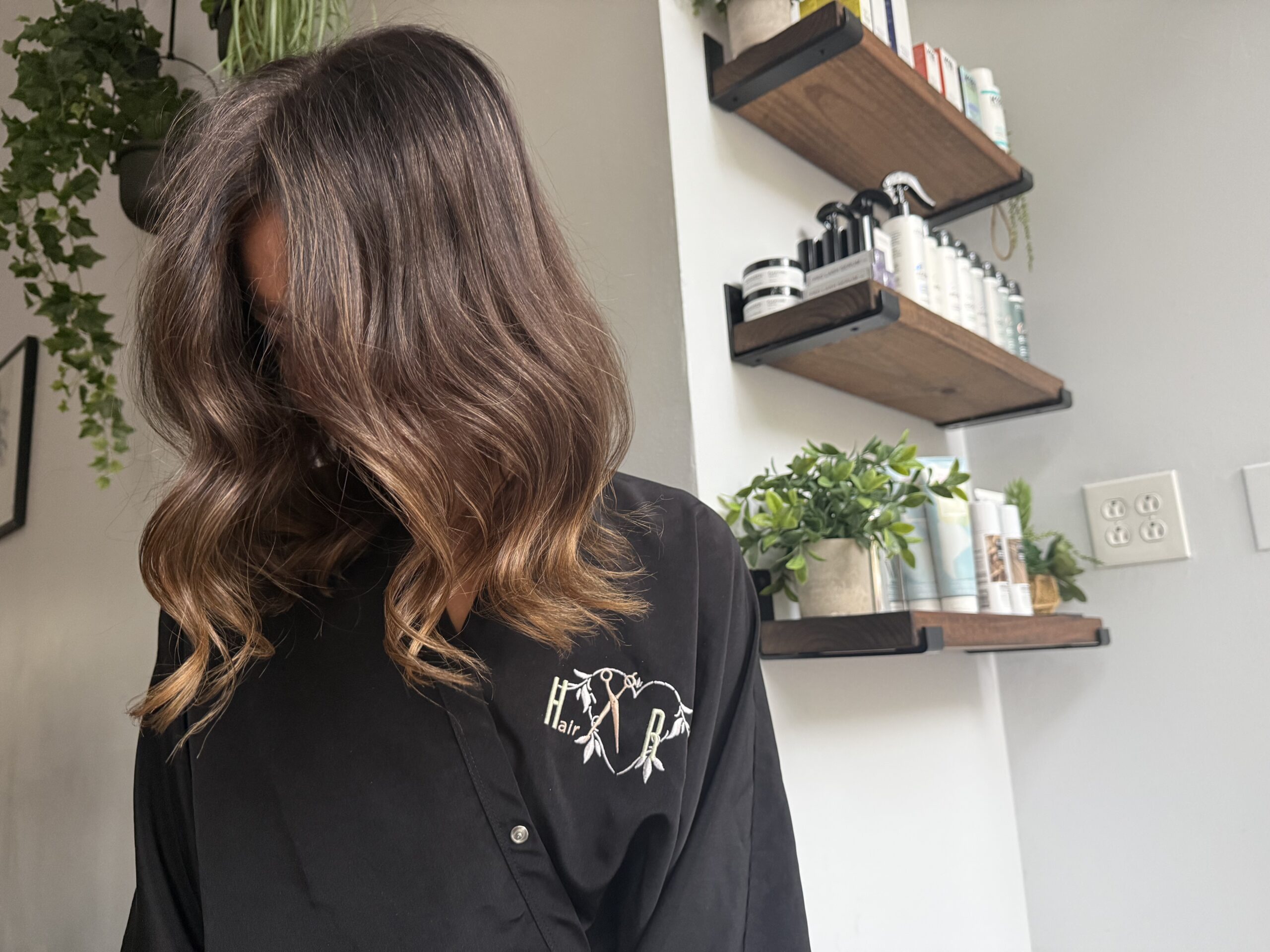 Woman with wavy brown hair in salon, wearing a black cape.