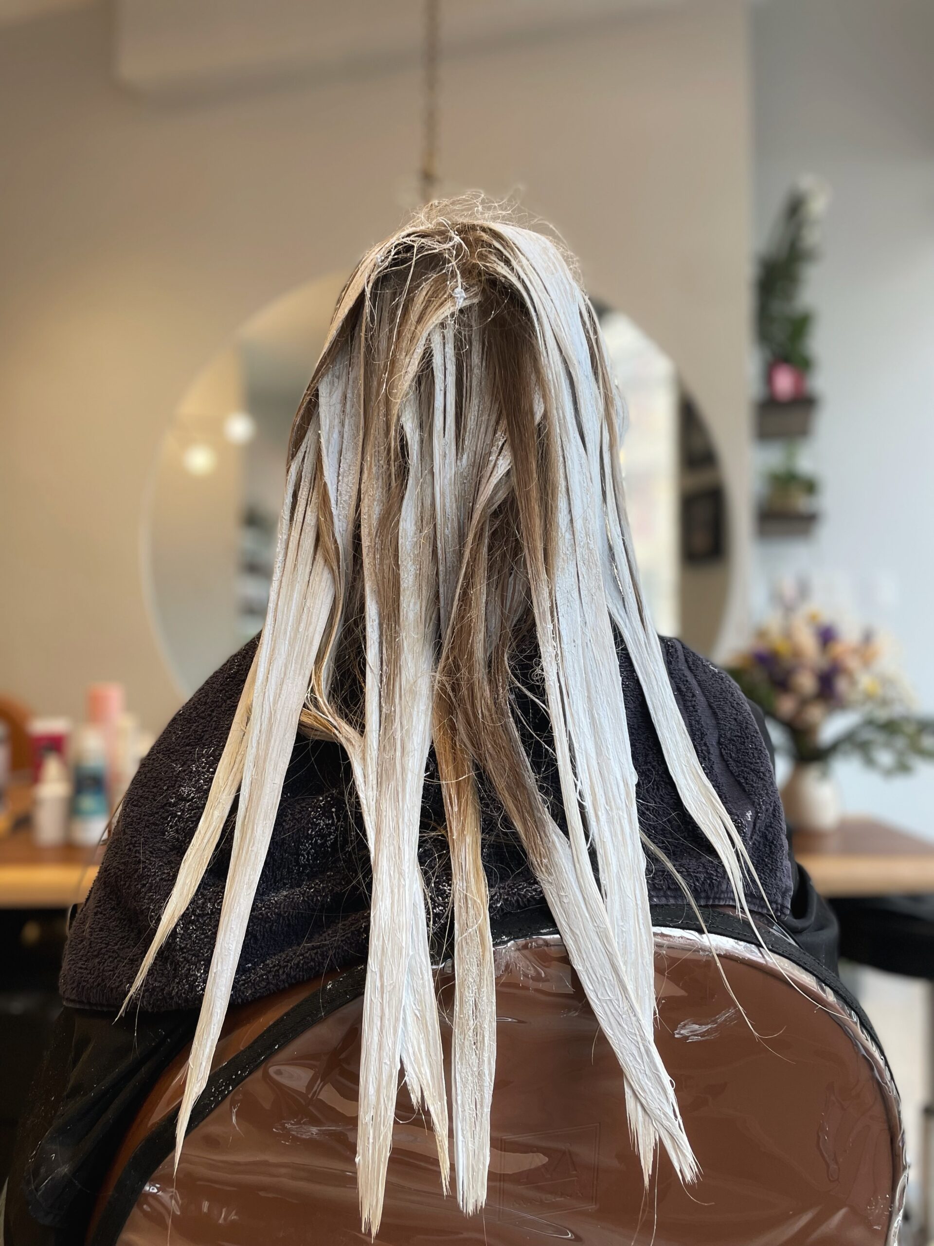 Person with long hair undergoing a hair coloring treatment in a salon.