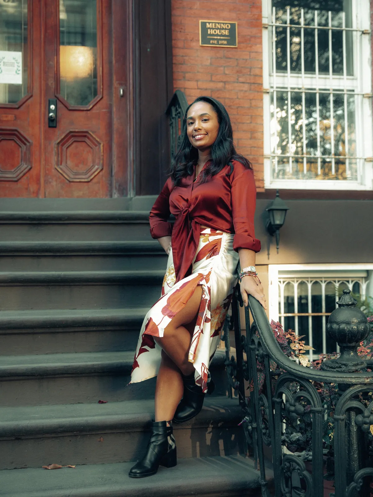 Woman in red blouse and patterned skirt poses on outdoor steps.