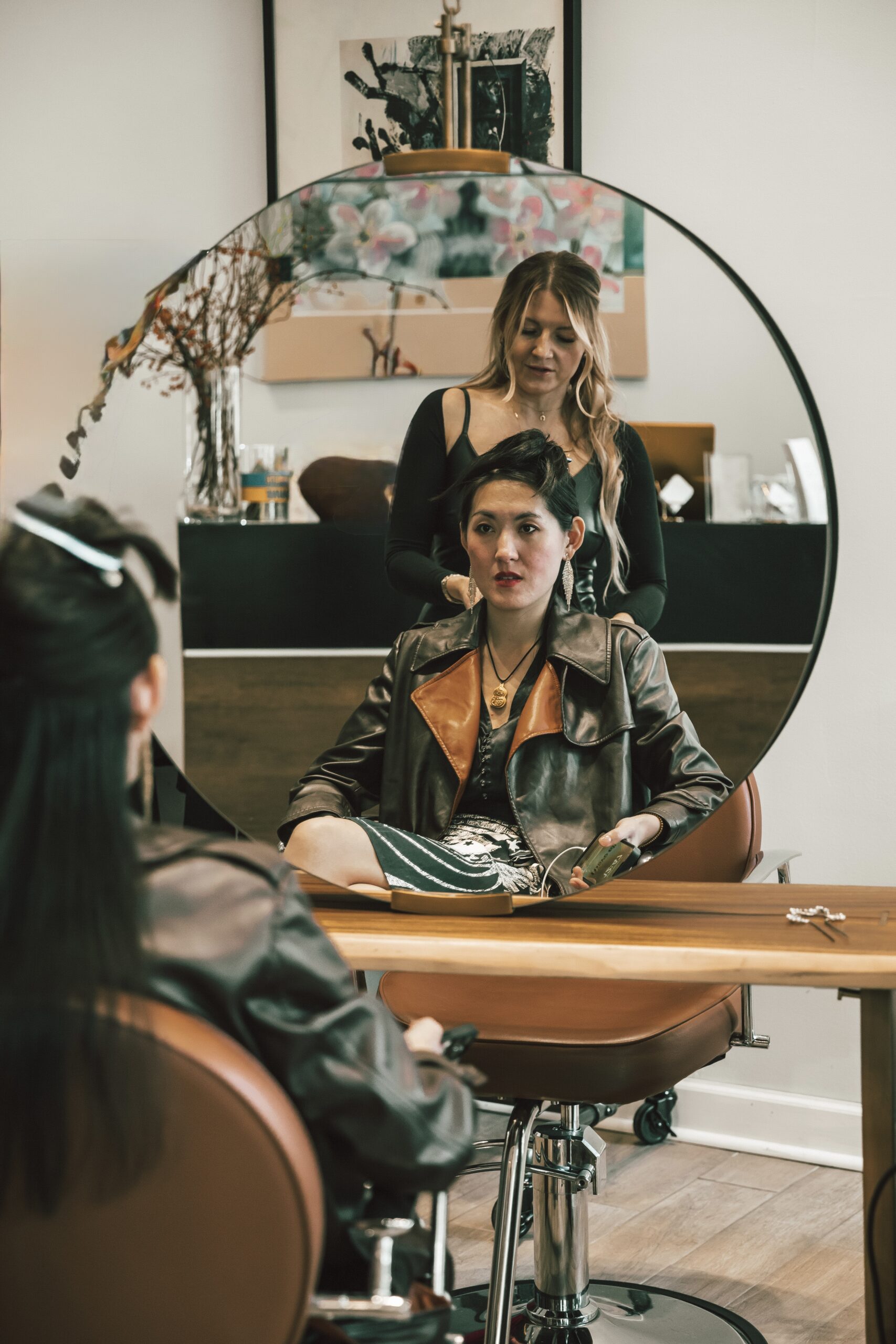 Woman in brown jacket seated at salon, stylist working on her hair.