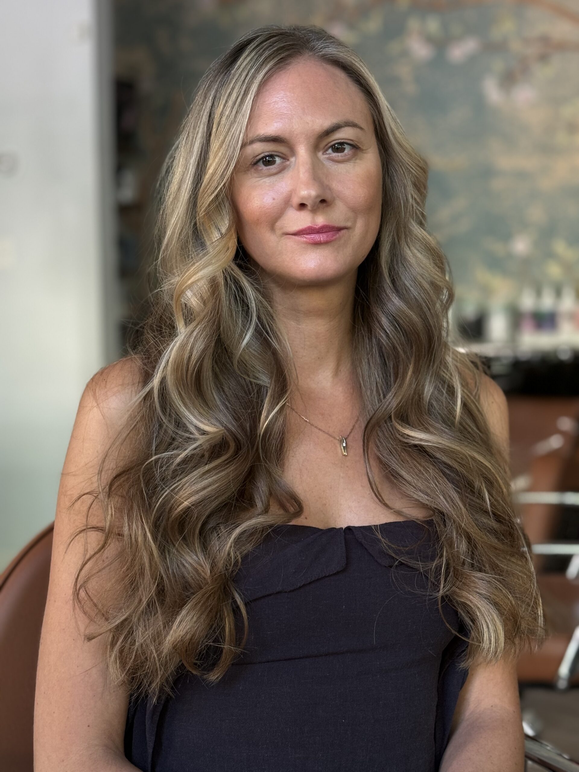 Woman with long, wavy hair wearing a black top in a salon setting.