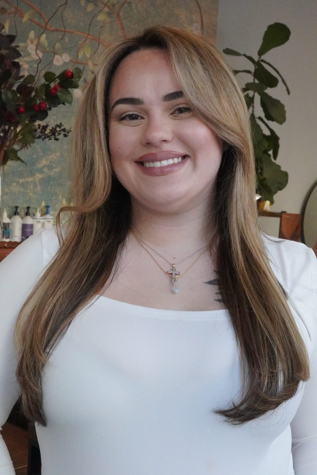 Smiling woman with long hair wearing a white top and a cross necklace.