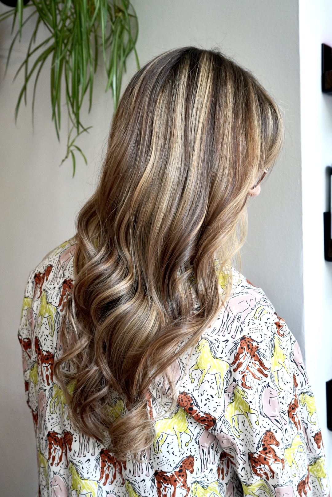 Woman with long, wavy hair wearing a patterned shirt featuring tigers and horses.
