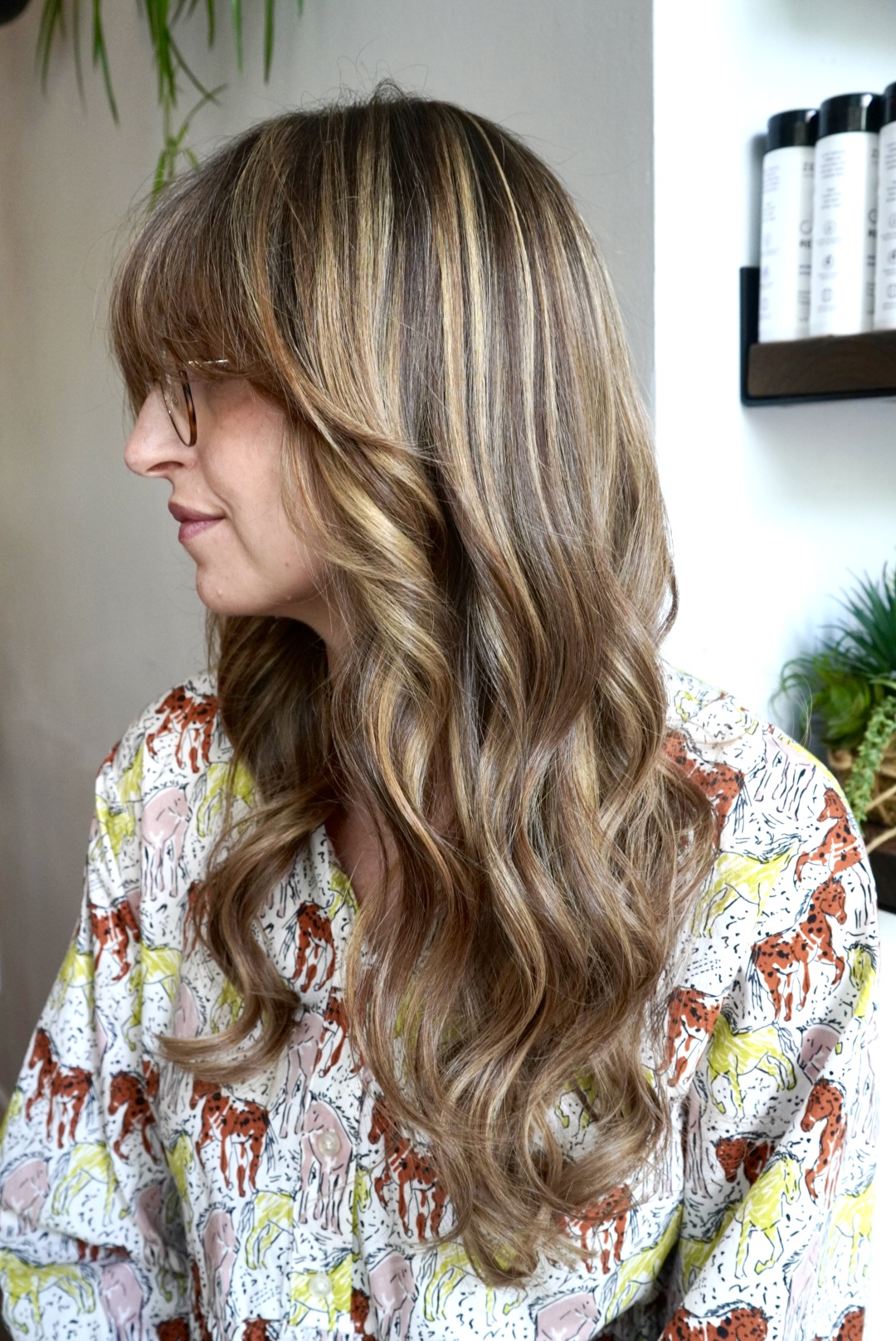 Woman with wavy, highlighted hair wearing glasses and a patterned shirt.